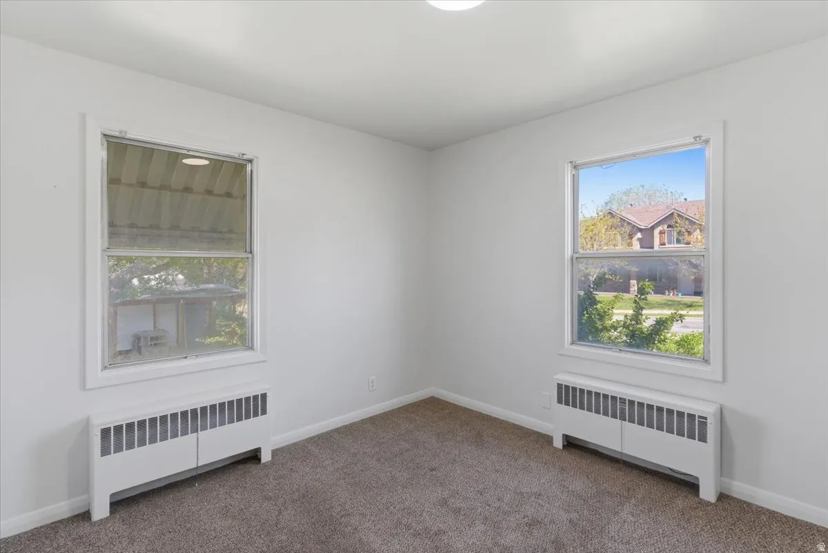 Carpeted room featuring two windows with white trim, two white radiator covers, and neutral-toned walls
