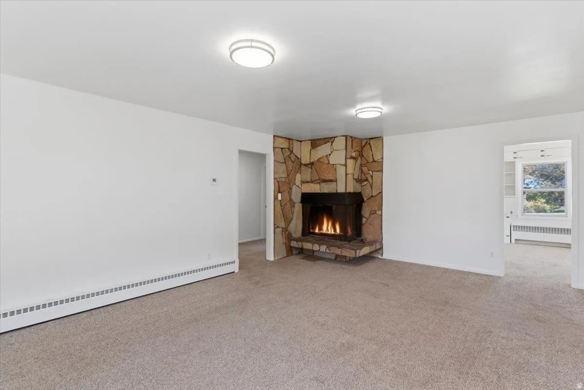 Living area featuring a corner stone-clad fireplace and neutral carpeting