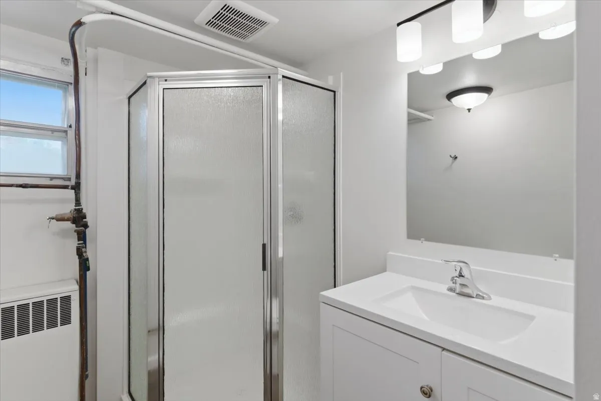 Bathroom featuring a corner shower with frosted glass enclosure, a single vanity with a white countertop and integrated sink, a rectangular mirror, and a multi-bulb vanity light fixture