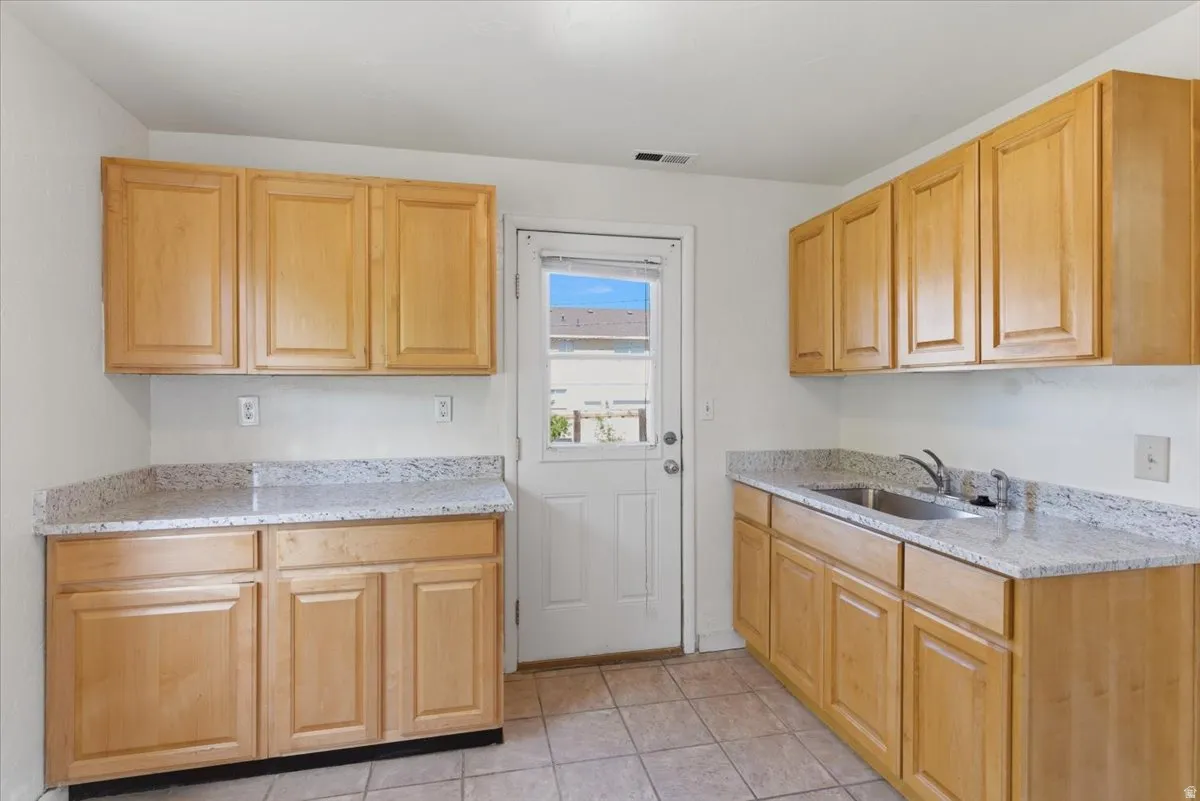 Kitchen featuring light wood cabinetry, granite-style countertops, stainless steel double basin sink, and ceramic tile flooring