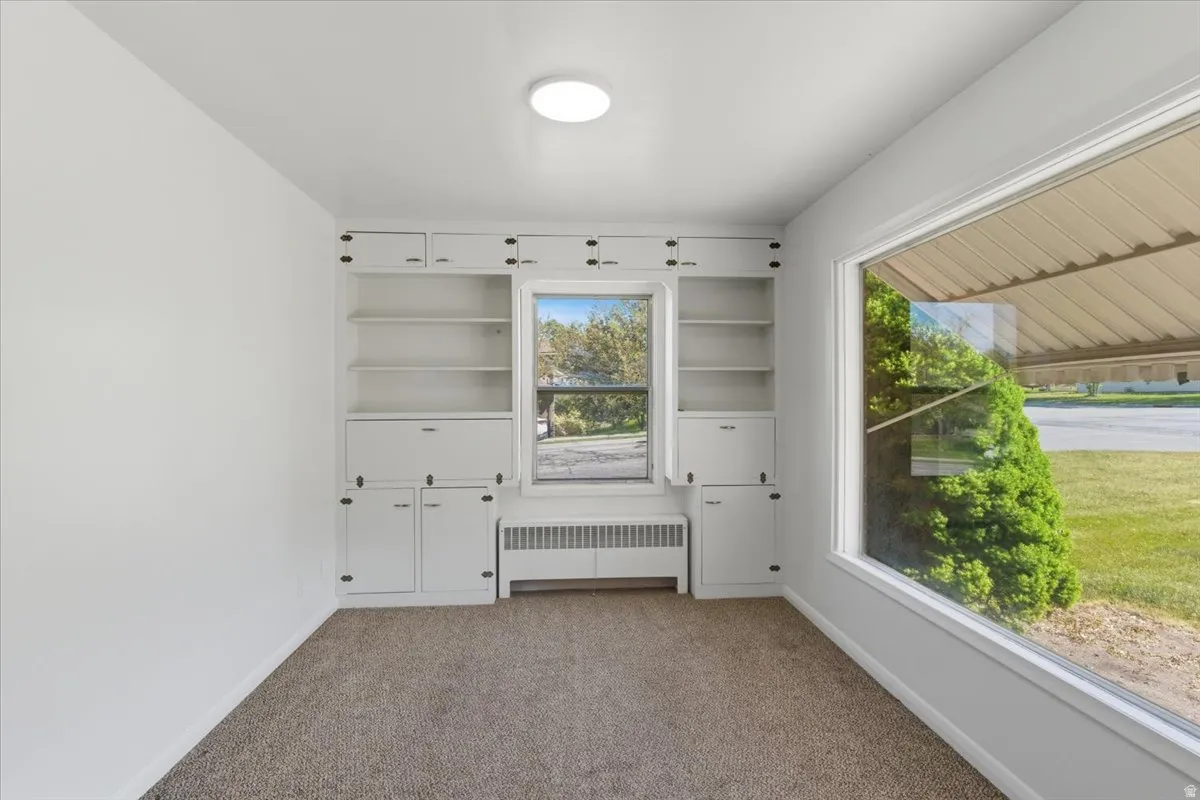 Bright interior room featuring a large picture window, built-in shelving, lower cabinetry, and plush carpeting
