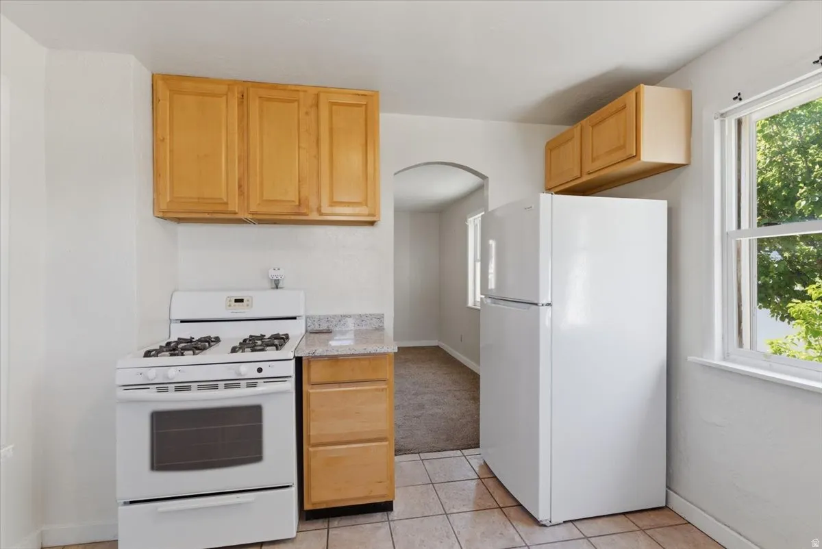 Kitchen featuring white appliances, light wood-finish cabinetry, a light-toned countertop, and tile flooring