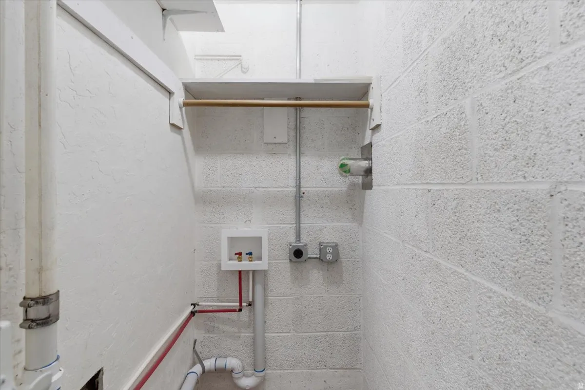Utility area featuring white-painted concrete block walls and exposed plumbing
