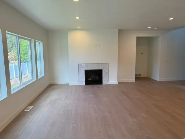 Recessed lighting, wood-finish flooring, white walls, multiple windows, and a fireplace with a white marble-look surround