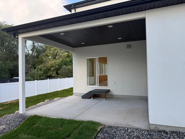 Covered concrete patio with recessed lighting, white stucco exterior, and a white vinyl privacy fence