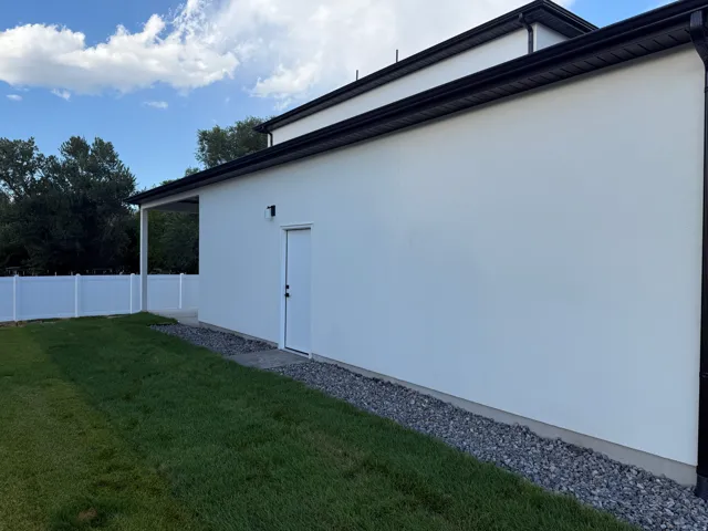 Exterior stucco finish with black gutters, covered patio, and a side access door