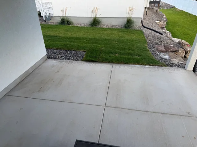 Concrete patio with a sod lawn, decorative gravel, and natural rock landscaping