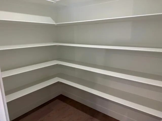 Expansive pantry featuring multiple levels of built-in shelving, white finishes, and wood-finish flooring