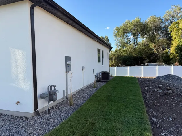 Smooth stucco exterior with black gutters, air conditioning unit, and white privacy fencing