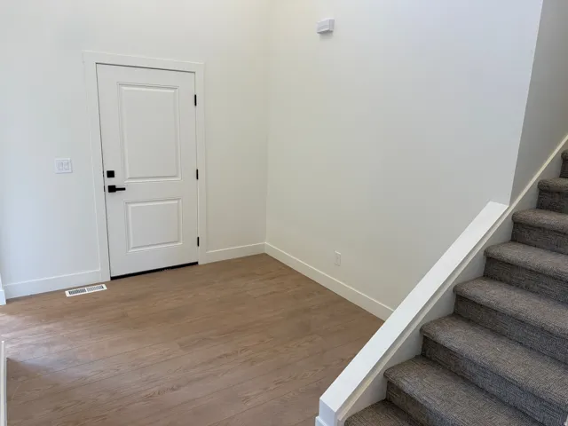 Panel door with matte black hardware, wood-finish flooring, and carpeted stairs