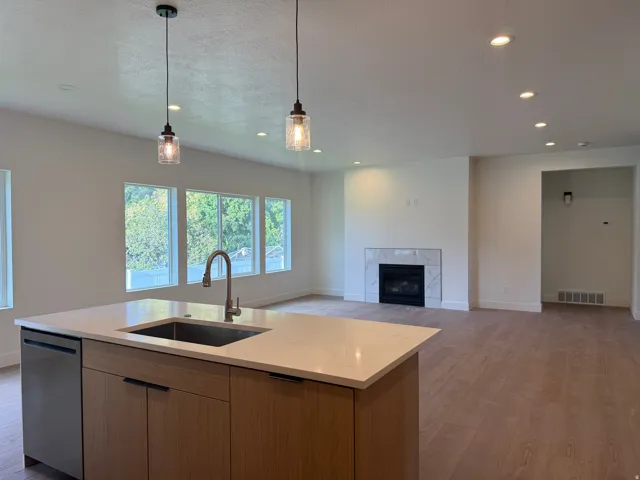 Open-concept interior featuring wood-finish flooring, a kitchen island with an undermount sink and integrated dishwasher, recessed lighting, and a fireplace with a tile surround