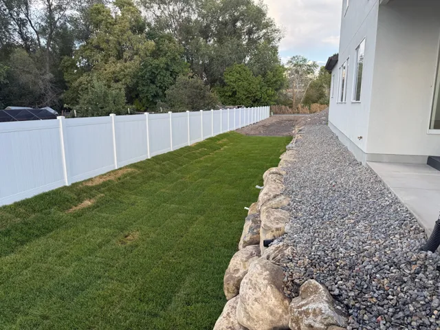 Private backyard with a vinyl fence, established lawn, and a rock retaining wall