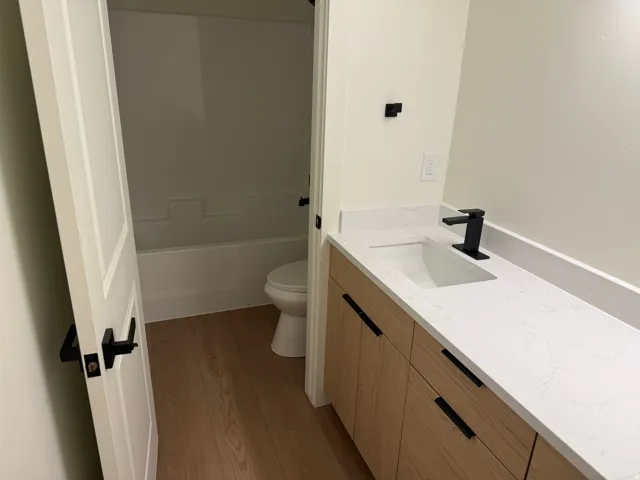 Modern vanity with integrated sink, wood-finish cabinetry, matte black hardware, and a white countertop