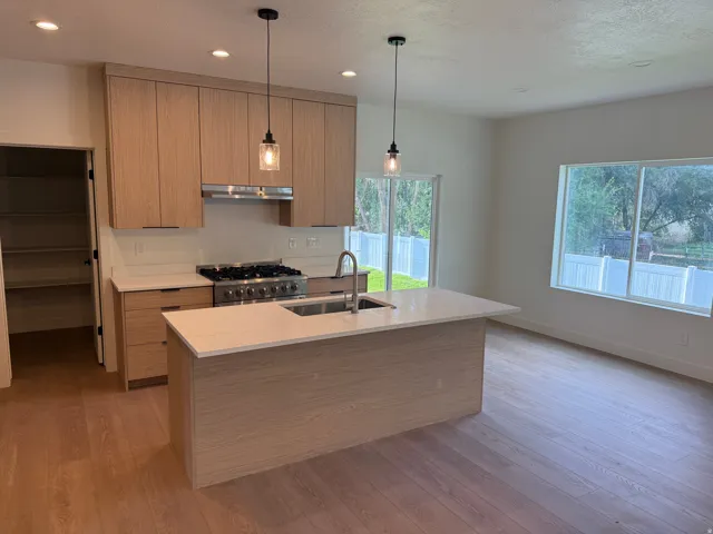 Kitchen featuring wood-finish cabinetry, stainless steel appliances, a center island with sink, recessed lighting, and wood-finish flooring