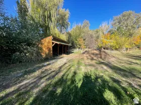 Open-sided wooden structure featuring a gabled roof, set amidst mature trees with vibrant autumn foliage