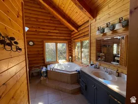 Log cabin interior featuring a built-in jetted tub, ceramic tile flooring, a dark wood-finish vanity with an integrated sink, and an expansive mirror