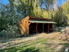 Wood-sided open-air shed with a green metal roof and exposed timber framing