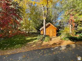 Wood-sided shed with double doors, set amongst mature trees with vibrant autumn foliage, and a landscaped garden bed