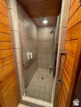 Shower with glass enclosure, beige tile walls, decorative accent tile band, and wood-paneled ceiling