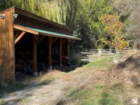 Wood-sided outbuilding with an extended covered area, supported by exposed timber framing, under a green metal roof
