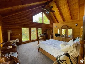 Vaulted wood plank ceiling with exposed beams, natural log wall construction, expansive window arrangement, and a ceiling fan