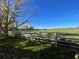 Expansive grassy field bordered by a wooden three-rail fence and mature trees