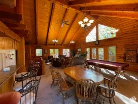 Spacious open-concept interior featuring vaulted wood-paneled ceilings, exposed wood beams, a prominent dining area, and multiple large windows