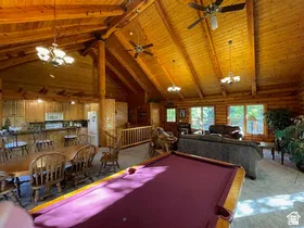 Spacious open-concept interior featuring vaulted wood ceilings with exposed beams, multiple ceiling fans, and a prominent billiards table