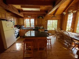 Open-concept kitchen and dining area featuring natural wood walls, wood-finish flooring, and exposed ceiling beams