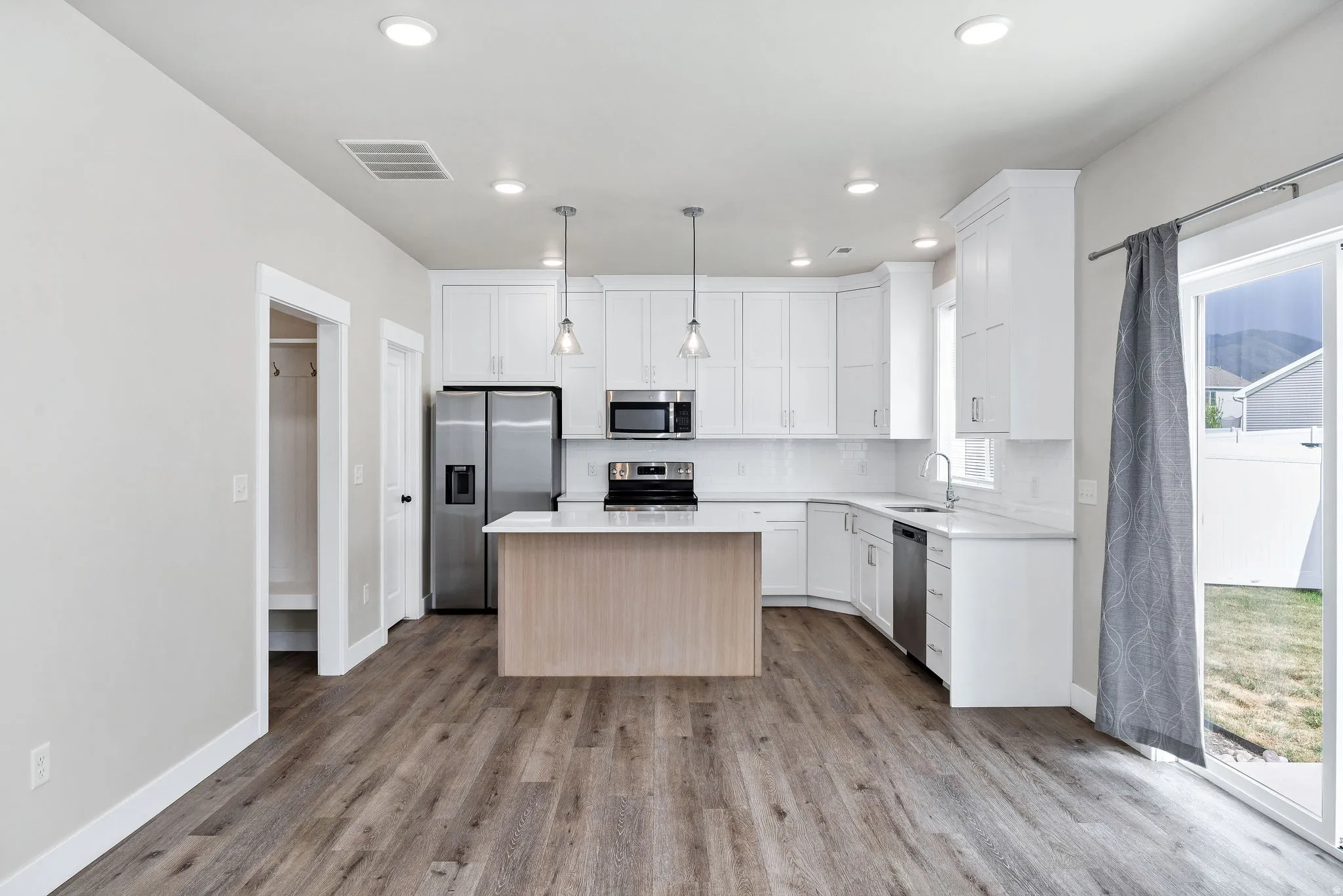 Open-concept kitchen featuring white cabinetry, stainless steel appliances, a center island with a light wood-finish base, pendant lighting, and wood-finish flooring