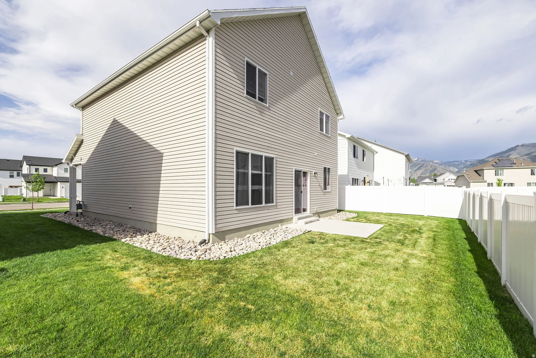 Rear exterior featuring light-colored horizontal siding, a private yard with a white vinyl fence, a concrete patio, and gravel landscaping along the foundation