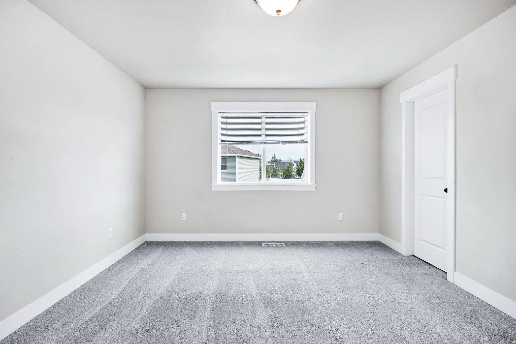 Neutral-toned room featuring a single window with blinds, light gray carpet, and white trim