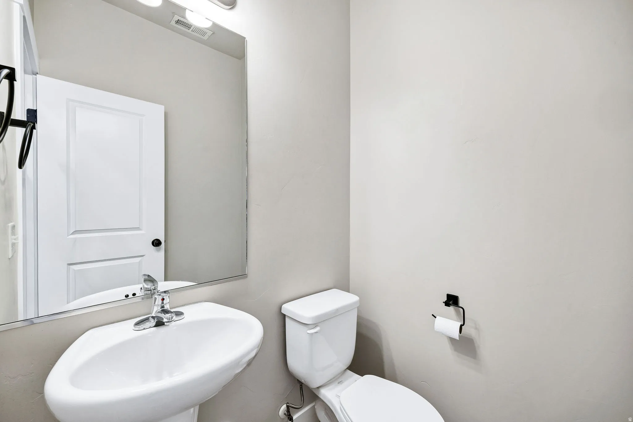 Pedestal sink with chrome faucet, toilet, and wall-mounted mirror