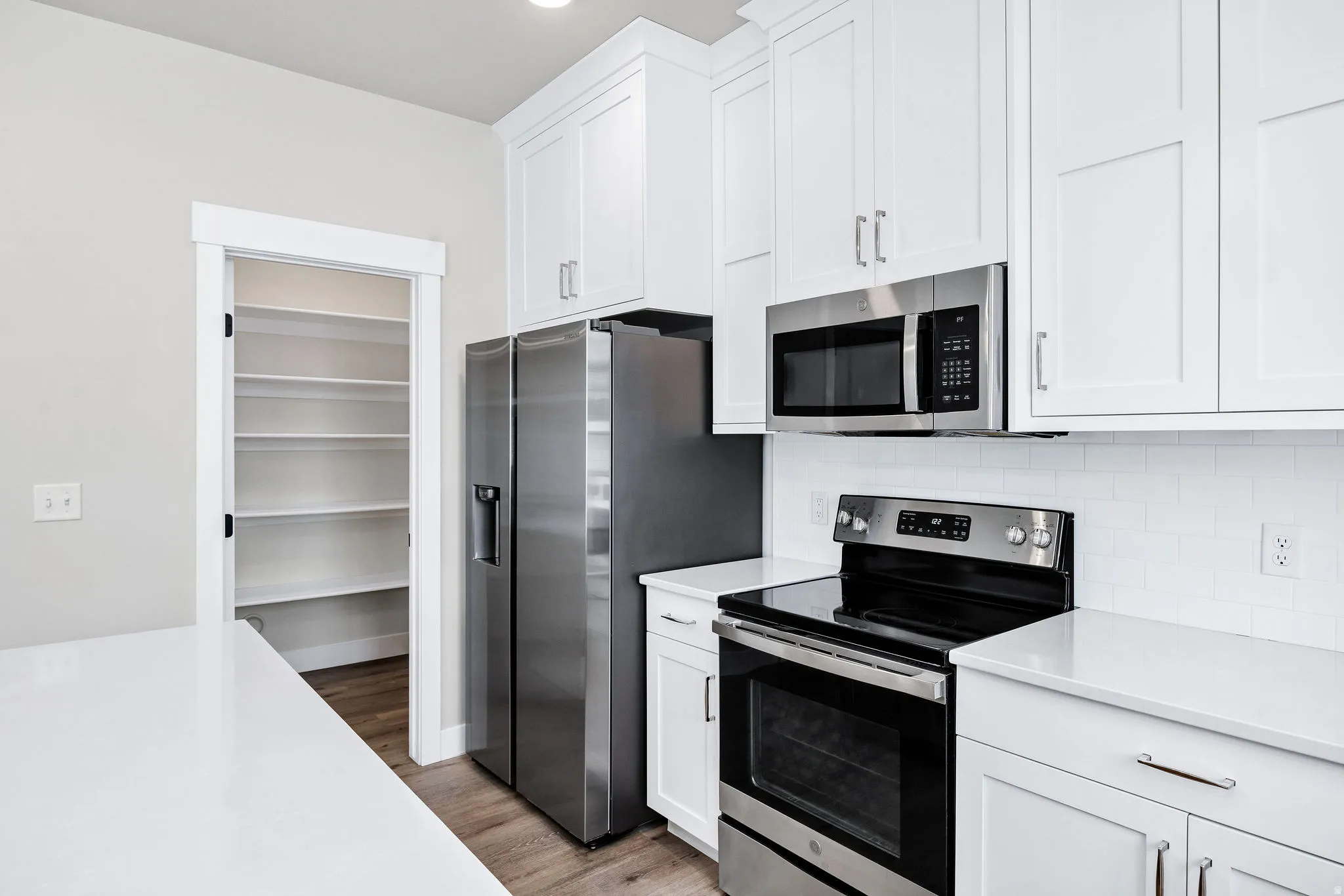 Modern kitchen featuring white shaker cabinetry, stainless steel appliances, white subway tile backsplash, and a spacious walk-in pantry