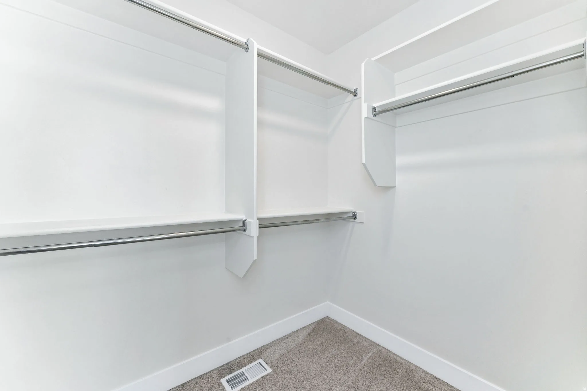 Bright closet space featuring built-in white shelving, chrome hanging rods, white baseboards, and carpet flooring