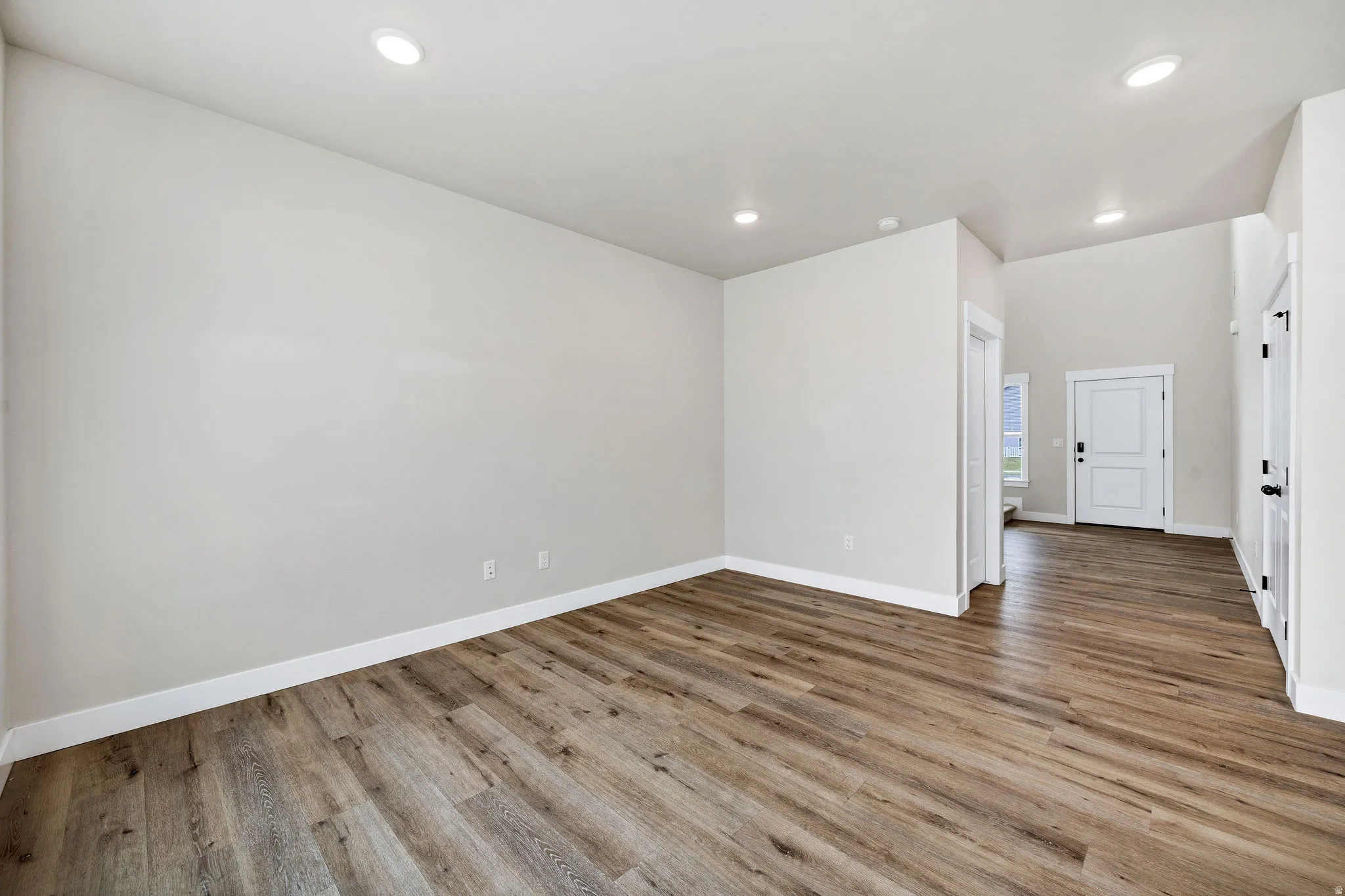 Spacious room featuring wood-finish flooring, recessed lighting, white trim, and light neutral wall paint