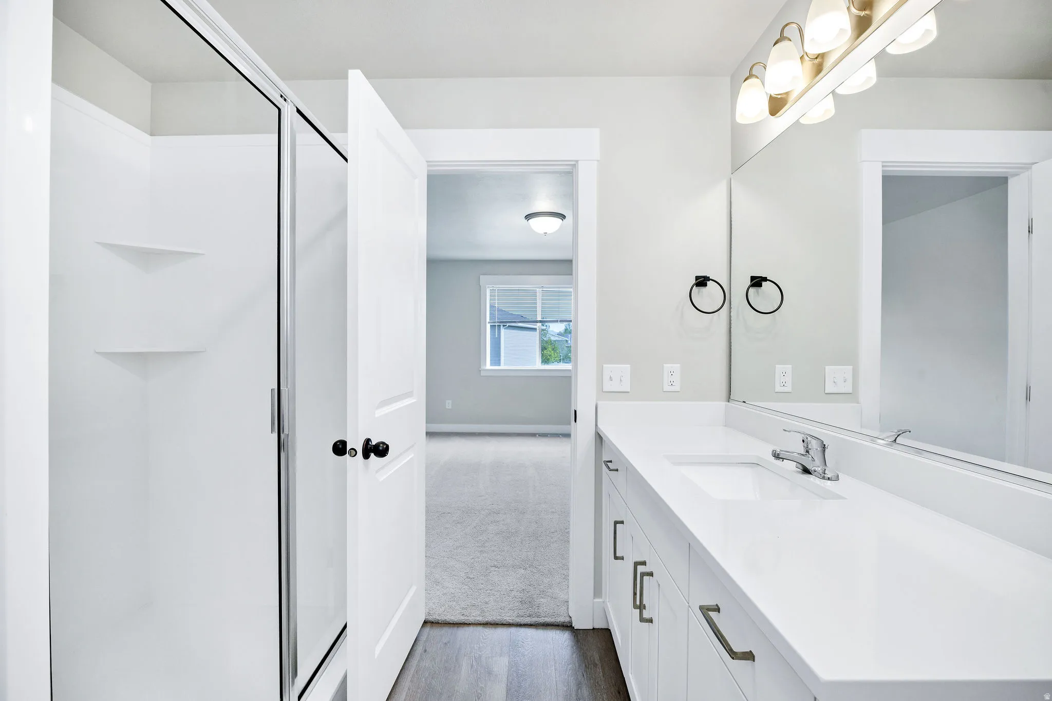 Bathroom featuring a white single-sink vanity with ample counter space and chrome faucet, an integrated shower with sliding glass door, and wood-finish flooring