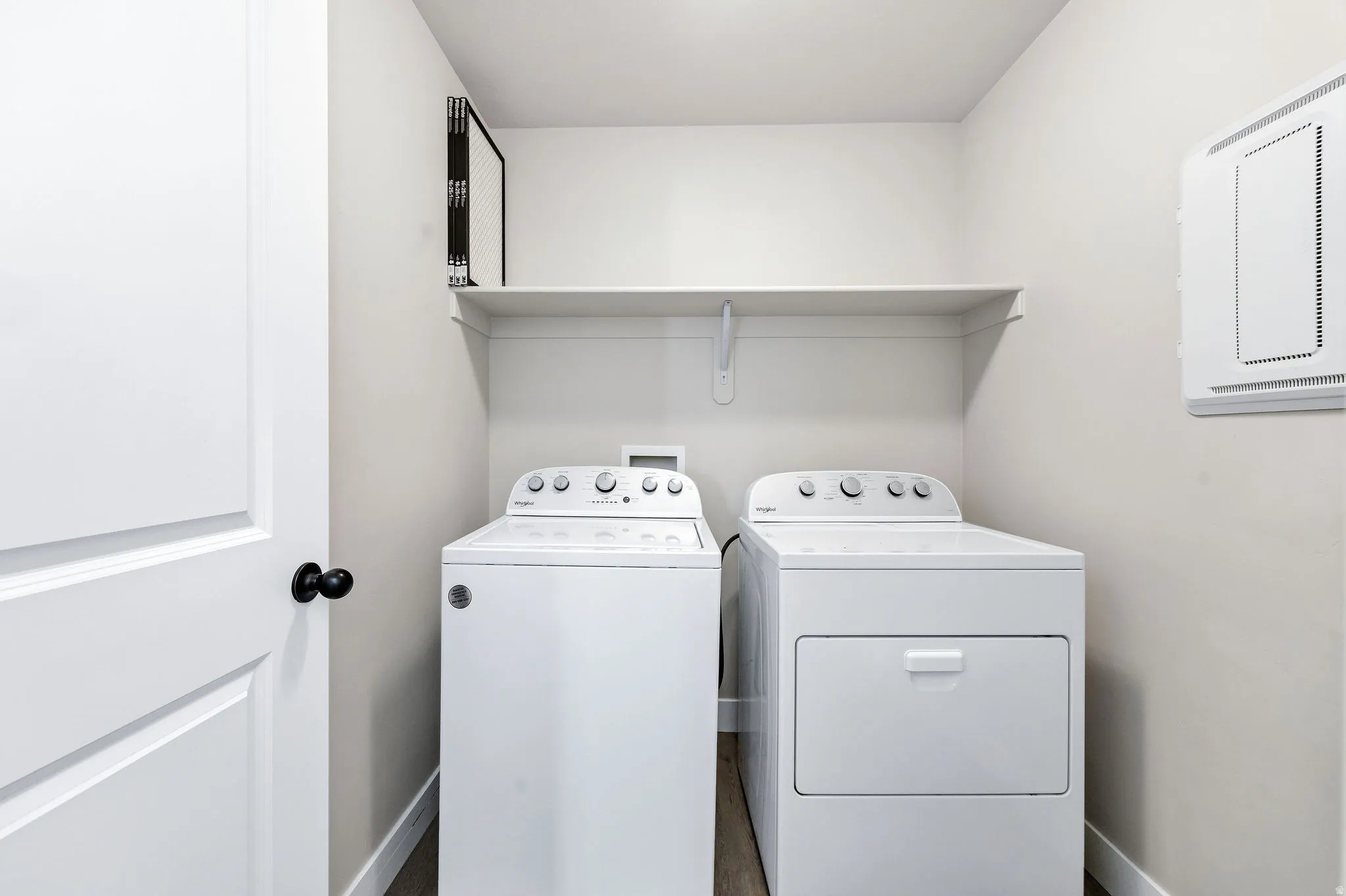 Dedicated utility area with wood-finish flooring, light neutral wall paint, and a white built-in storage shelf