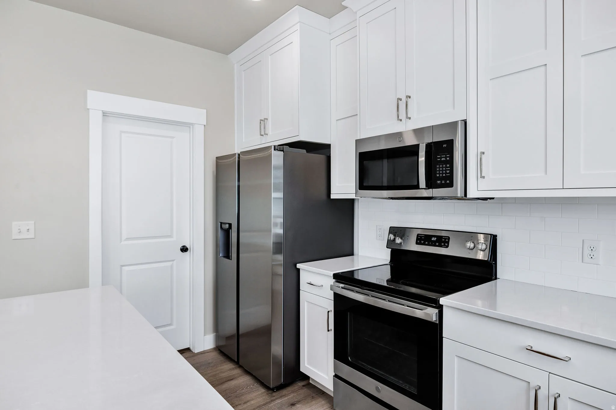 Contemporary kitchen featuring white shaker cabinetry, stainless steel appliances, white subway tile backsplash, light wood-finish flooring, and light-toned countertops