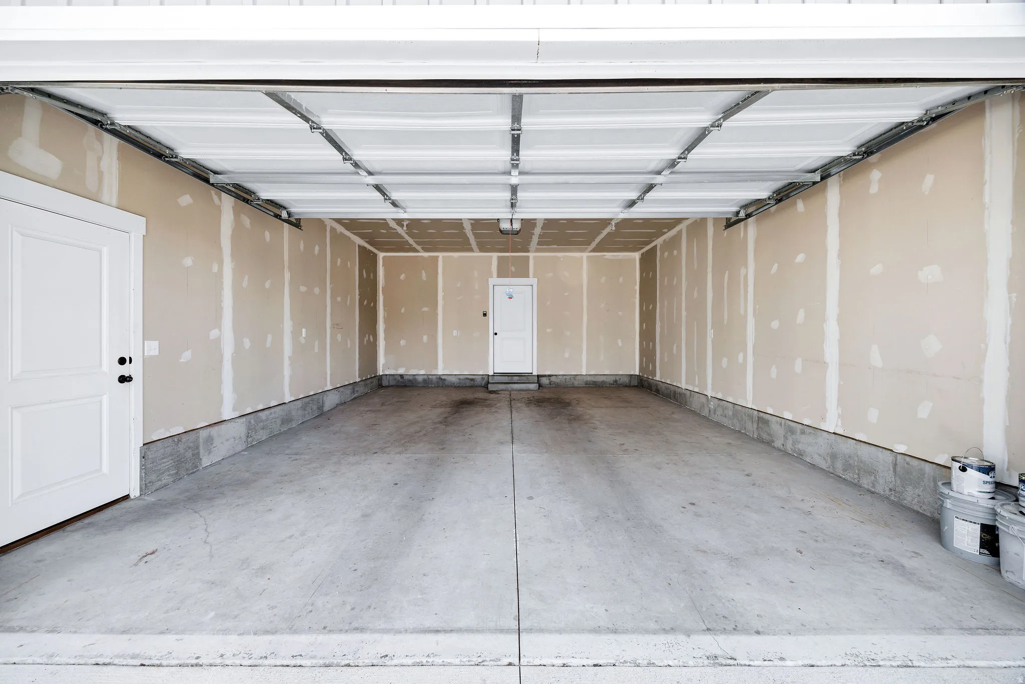 Spacious garage interior featuring an overhead door mechanism, concrete flooring, and unfinished drywall