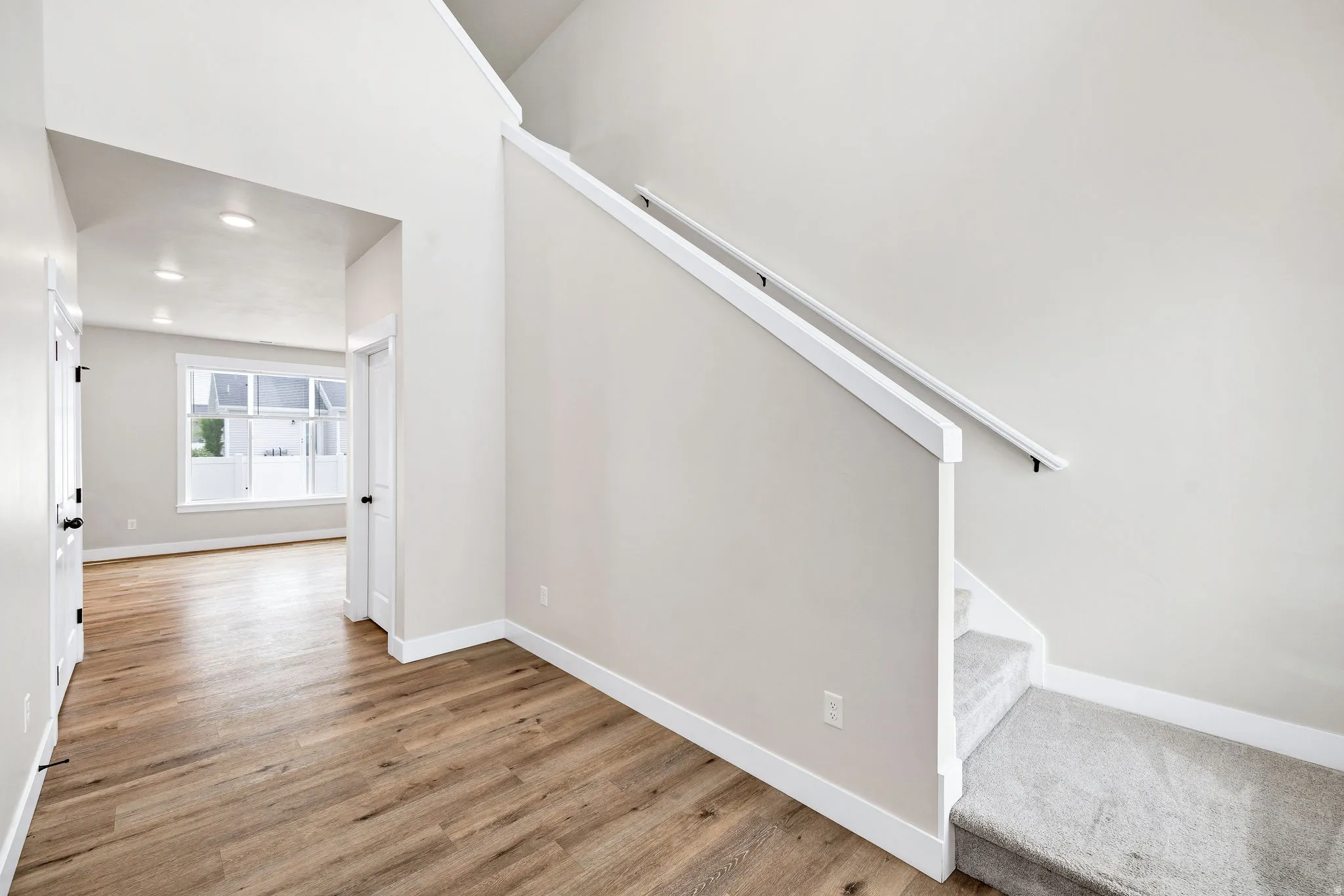 Entryway featuring wood-finish flooring, a carpeted staircase with white trim, and a high vaulted ceiling