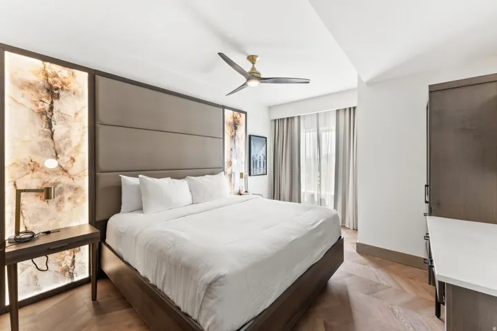 Bedroom featuring a padded headboard with illuminated onyx accent panels, wood-finish herringbone flooring, and a ceiling fan