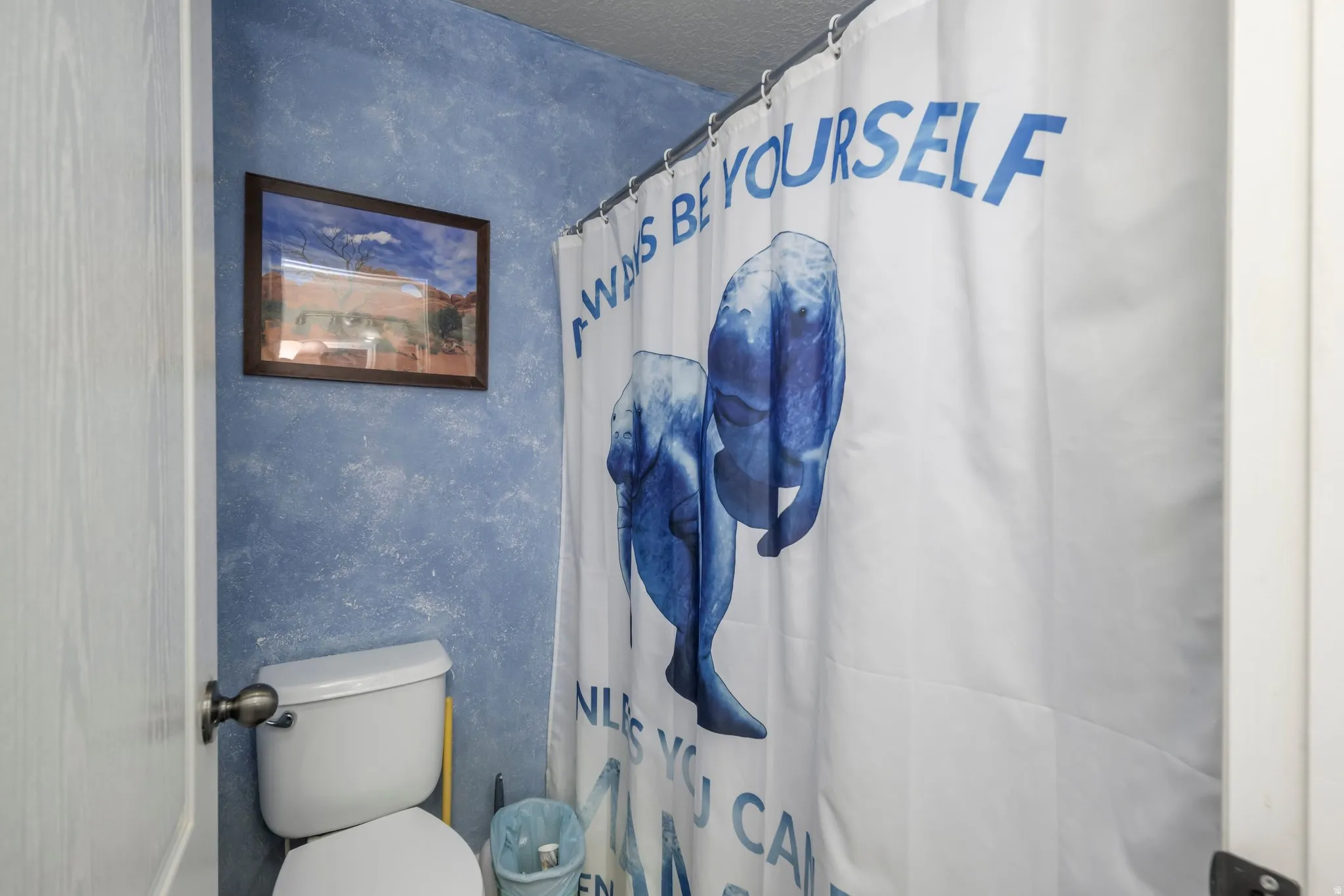 Bathroom featuring a white toilet, textured blue wall finish, and a shower area with a white shower curtain