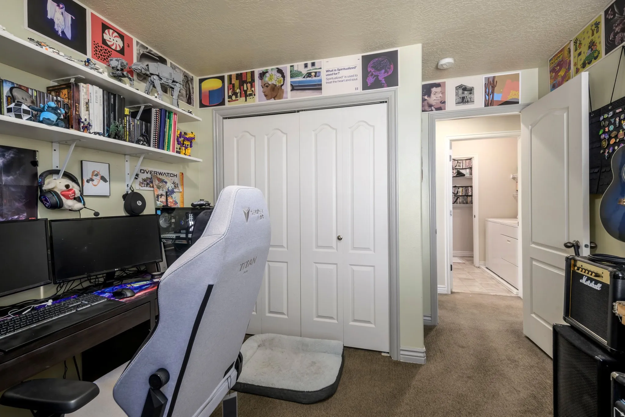 Carpeted room featuring a double bifold closet, built-in wall shelving, and a doorway opening to an additional room with tile flooring and a built-in appliance
