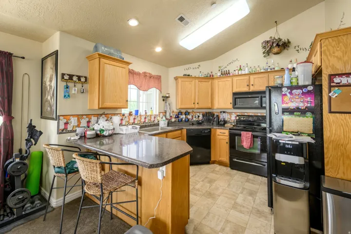 Kitchen featuring wood-finish cabinetry, black appliances, a granite-finish countertop, a built-in double basin sink, and recessed lighting