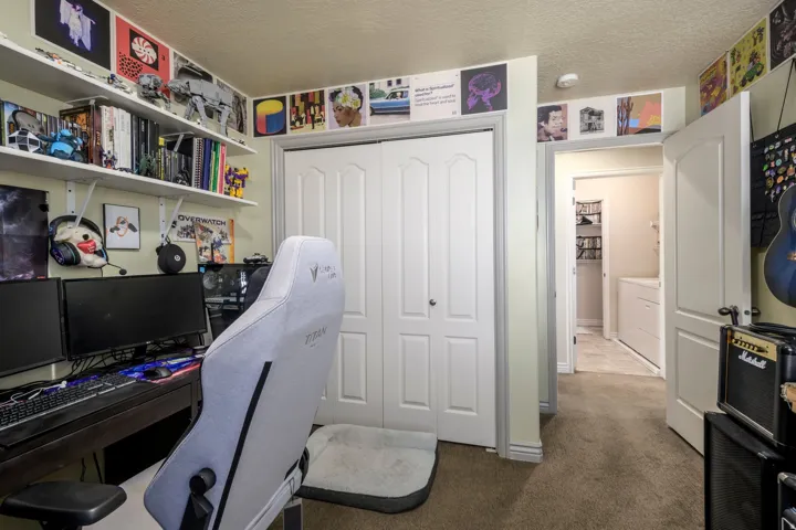 Carpeted room featuring a double bifold closet, built-in wall shelving, and a doorway opening to an additional room with tile flooring and a built-in appliance