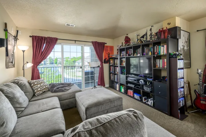 Living space featuring a sliding glass door, balcony with metal railings, built-in shelving unit, and wall-to-wall carpeting