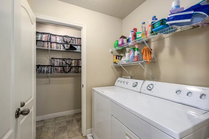 Dedicated laundry area featuring a white top-load washer and dryer, wall-mounted wire shelving, and neutral wall paint