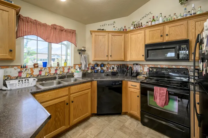 Kitchen featuring wood-finish cabinetry, black appliances, a double basin stainless steel sink, and a window above the sink