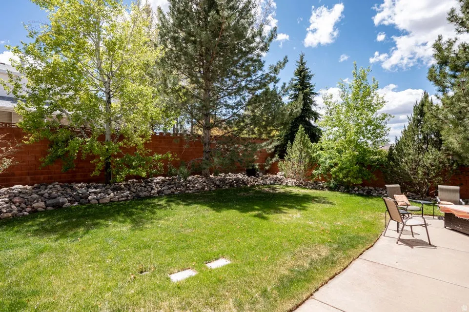 Expansive backyard featuring a lush lawn, mature trees, a red brick privacy fence, and a flagstone border
